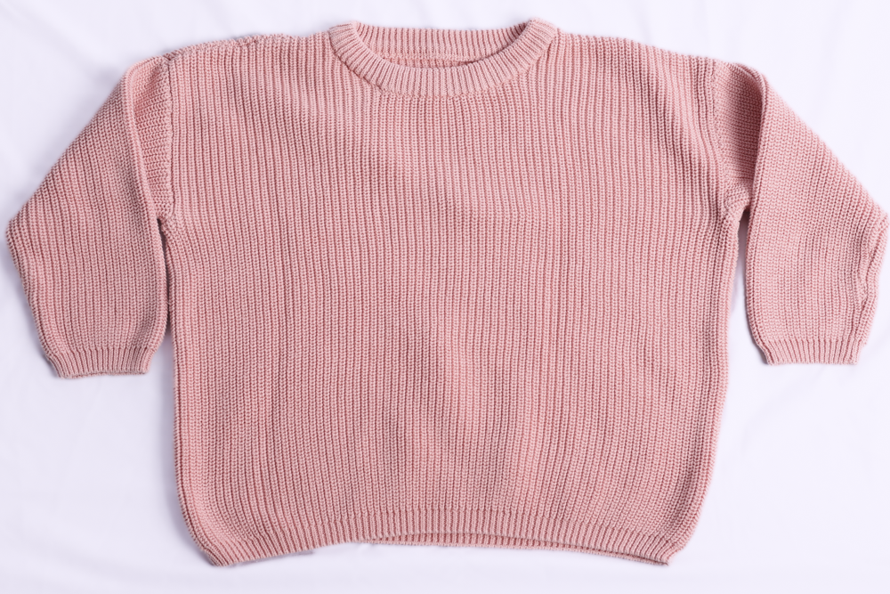 A pink ribbed knit crewneck sweater with long sleeves, laid flat on a white background.