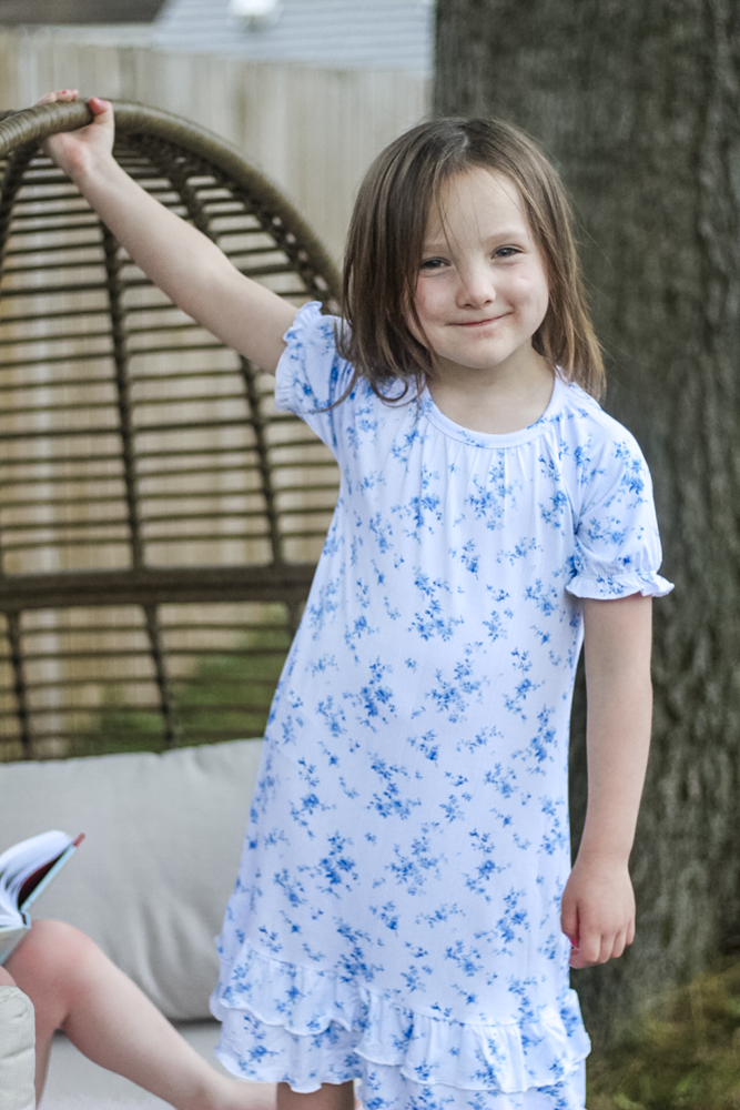A young girl wearing a white short-sleeve bamboo nightgown with a blue floral print. 