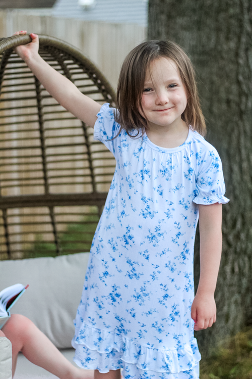 A young girl wearing a white short-sleeve bamboo nightgown with a blue floral print. 