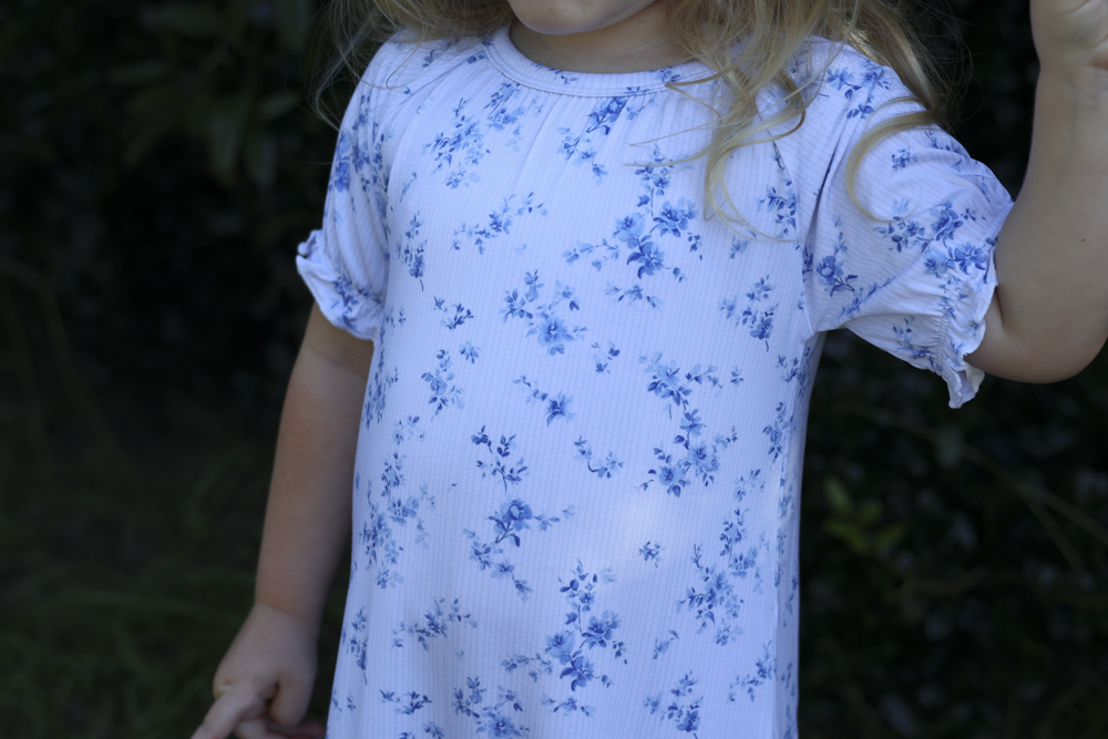 A child wearing a white short-sleeve bamboo nightgown with a blue floral print, photographed outdoors against a dark blurred background.