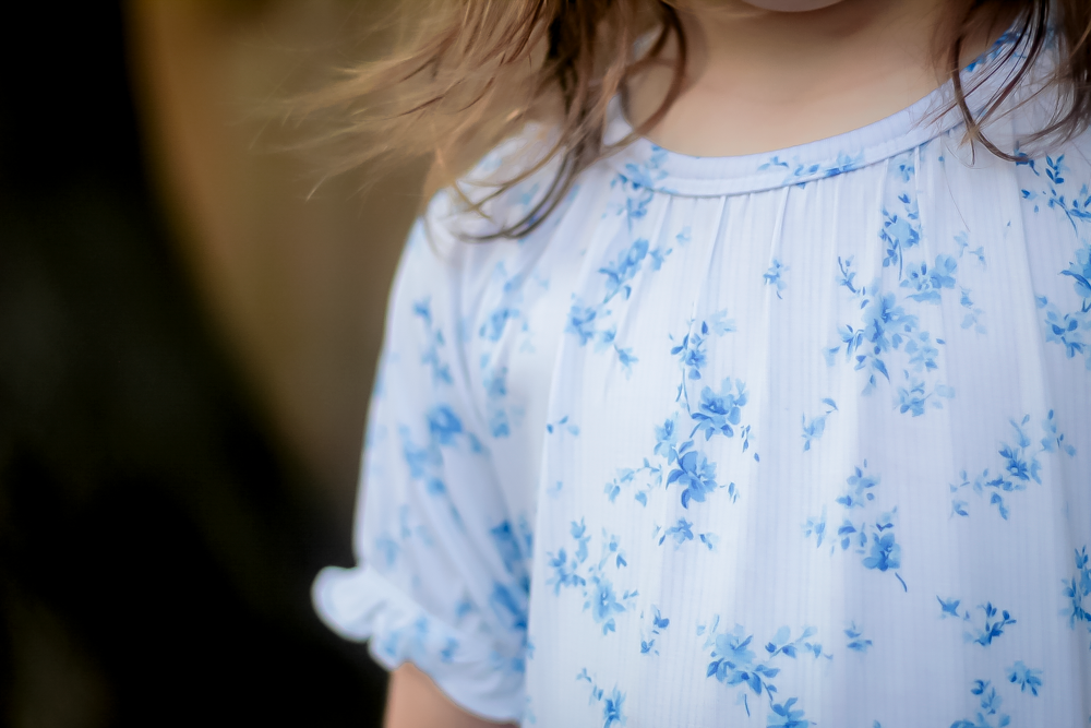 Close-up of a child wearing a white short-sleeve bamboo nightgown with a blue floral print, featuring a gathered neckline and ruffled sleeves.
