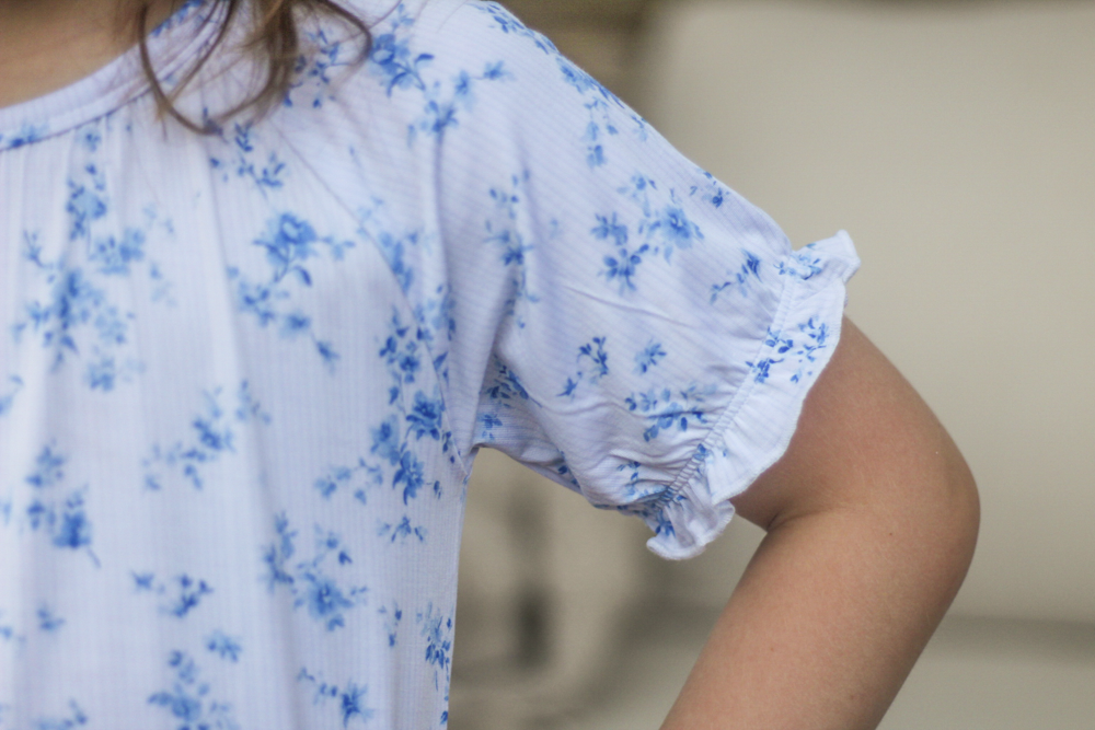 Close-up of a person wearing a white short-sleeve bamboo nightgown with a blue floral print and ruffled puff sleeves.