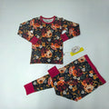 A two-piece children's pajama set laid flat on a white background, featuring a long-sleeve top and matching pants with a dark floral print, coordinating dark red cuffs, and collar.